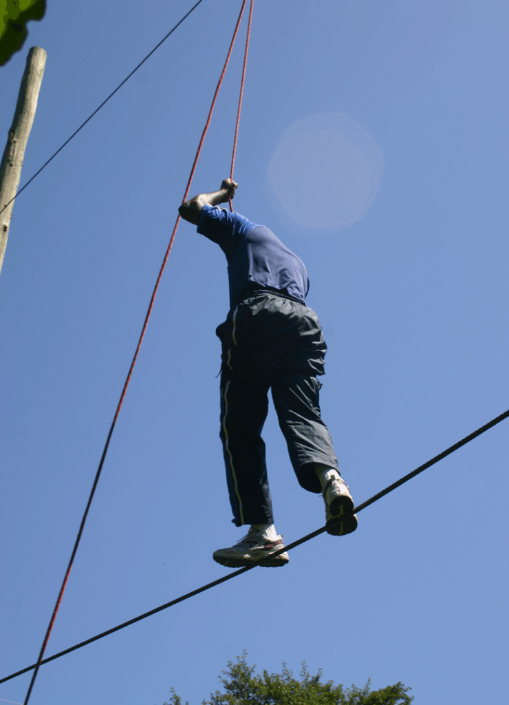 Participant completing a high-ropes balance challenge during an outdoor The Ventures Group teambuilding activity.